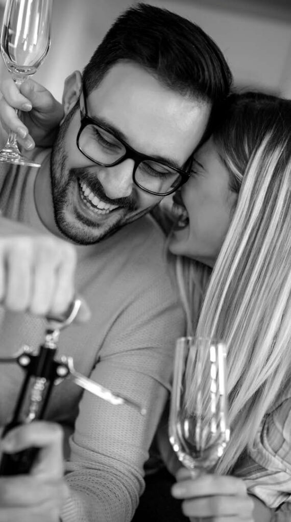 A happy couple enjoying a unique urban experience, sharing a moment of laughter while holding wine glasses. The man is opening a bottle of wine, capturing a relaxed and joyful atmosphere