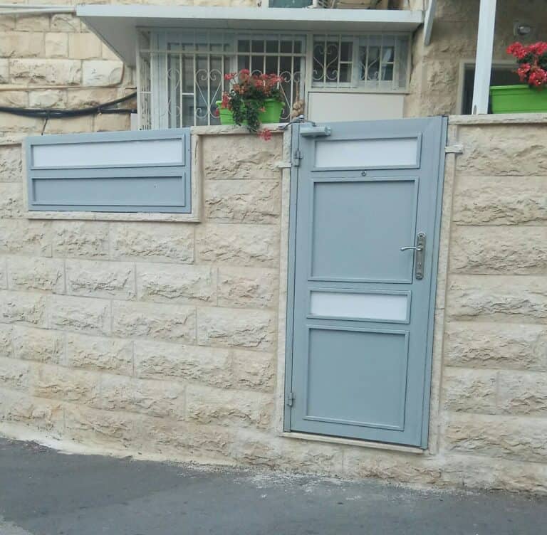 A light blue door with a window above it, set in a stone wall with a potted plant on the windowsill.
