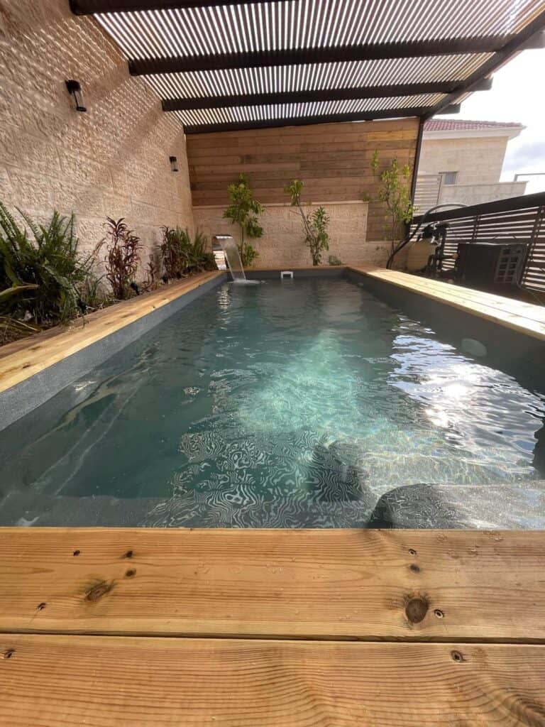 Modern backyard pool with wooden deck and plants.