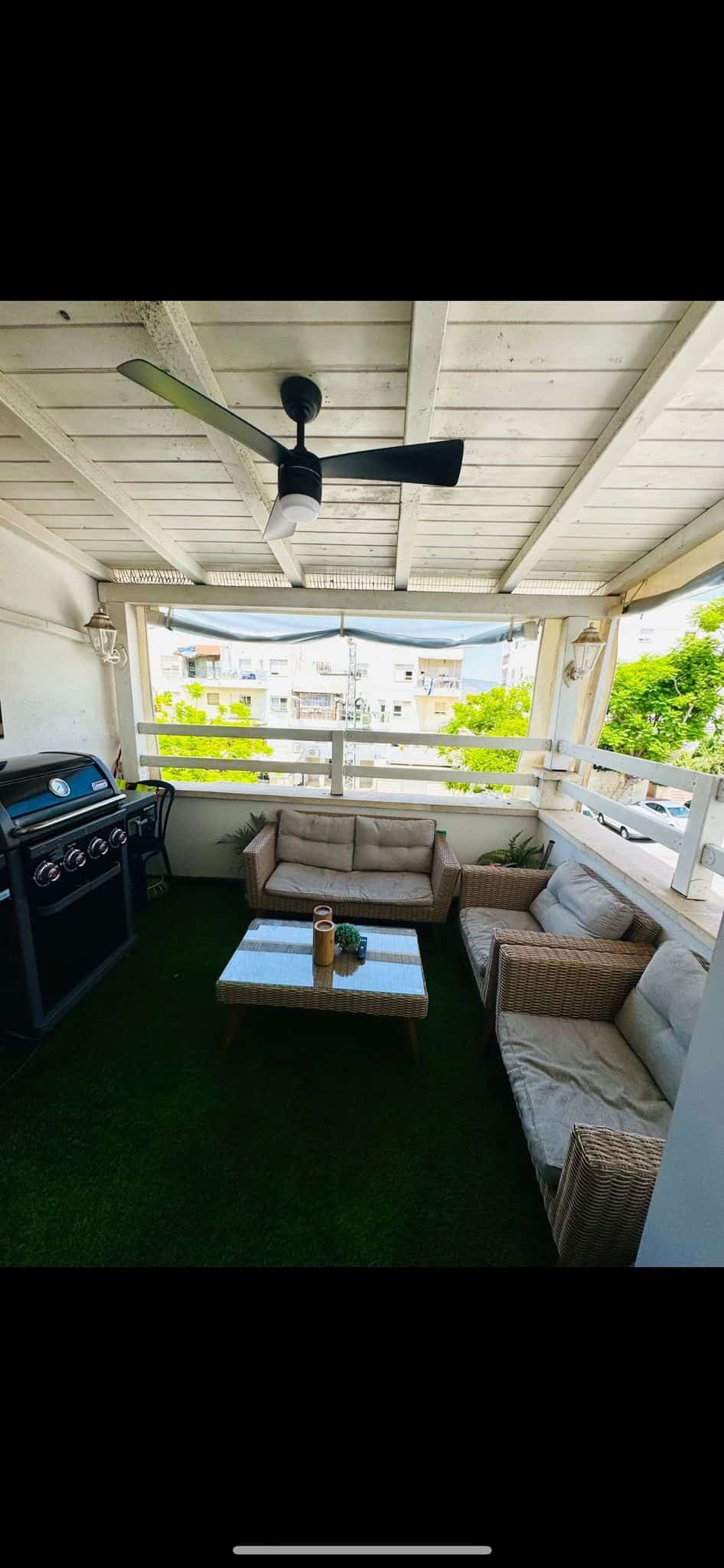 Patio furniture on a balcony with grill and greenery.