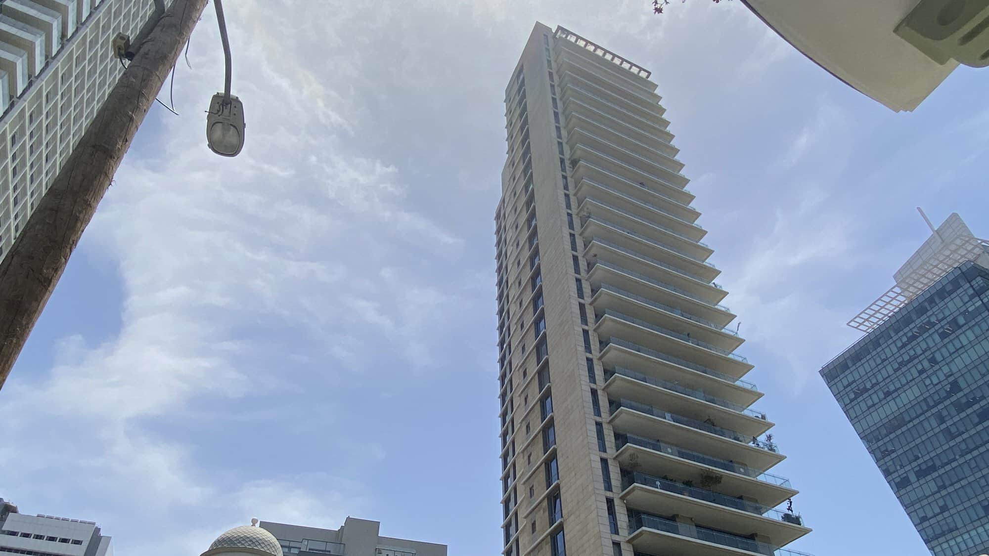 A tall apartment tower with balconies on Allenby Street in Tel Aviv, seen against the sky.