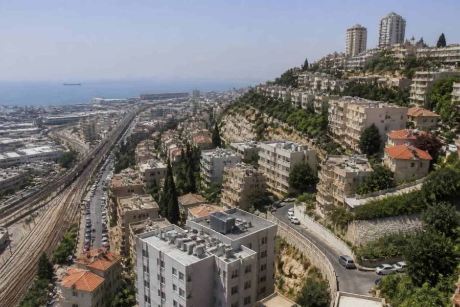 Photorealistic view of Haifa apartment buildings on a hillside with modern urban infrastructure and the Mediterranean coast in the distance