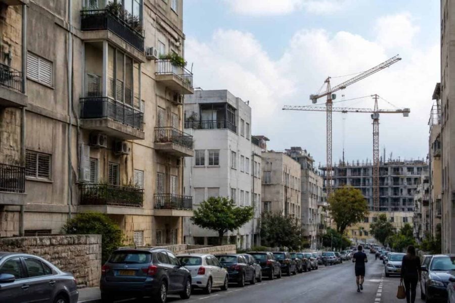 Older apartment buildings on an Israeli residential street with new construction in the background
