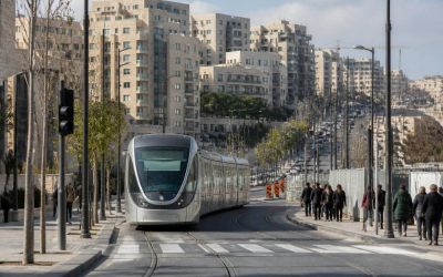 Jerusalem light rail train passing through a modern urban neighborhood with apartment buildings and pedestrians nearby