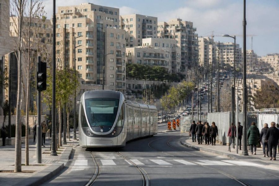 Jerusalem light rail train passing through a modern urban neighborhood with apartment buildings and pedestrians nearby