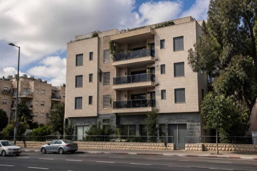 Exterior of a modest apartment building with balconies on a Jerusalem residential street