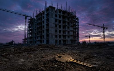 A half-finished concrete apartment block at blue-hour dusk, scaffolding bare and the cranes idle, exposed rebar against a bruised violet sky, and in the dirt of the foreground a single oversized brass door key lying abandoned and slightly buried, soft cold light catching its edge, shot wide on a 24mm lens with deep focus, quiet and unsettling, a sense of a promise left unbuilt. No text, no words, no numbers, no logos anywhere in the image.
