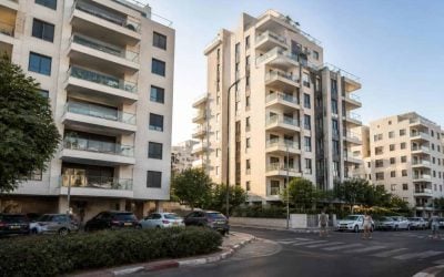 Modern apartment buildings along an Israeli coastal city street with pedestrians and parked cars