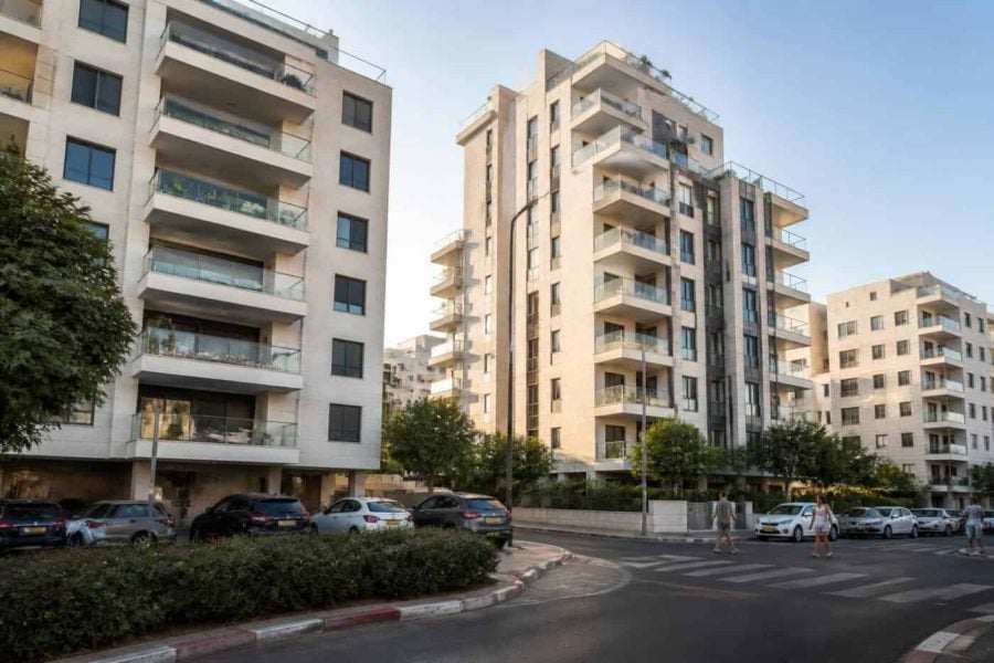 Modern apartment buildings along an Israeli coastal city street with pedestrians and parked cars