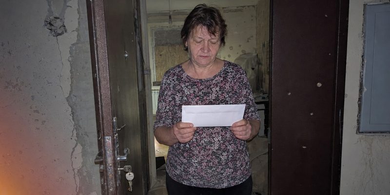 woman receives official letter in war damaged home